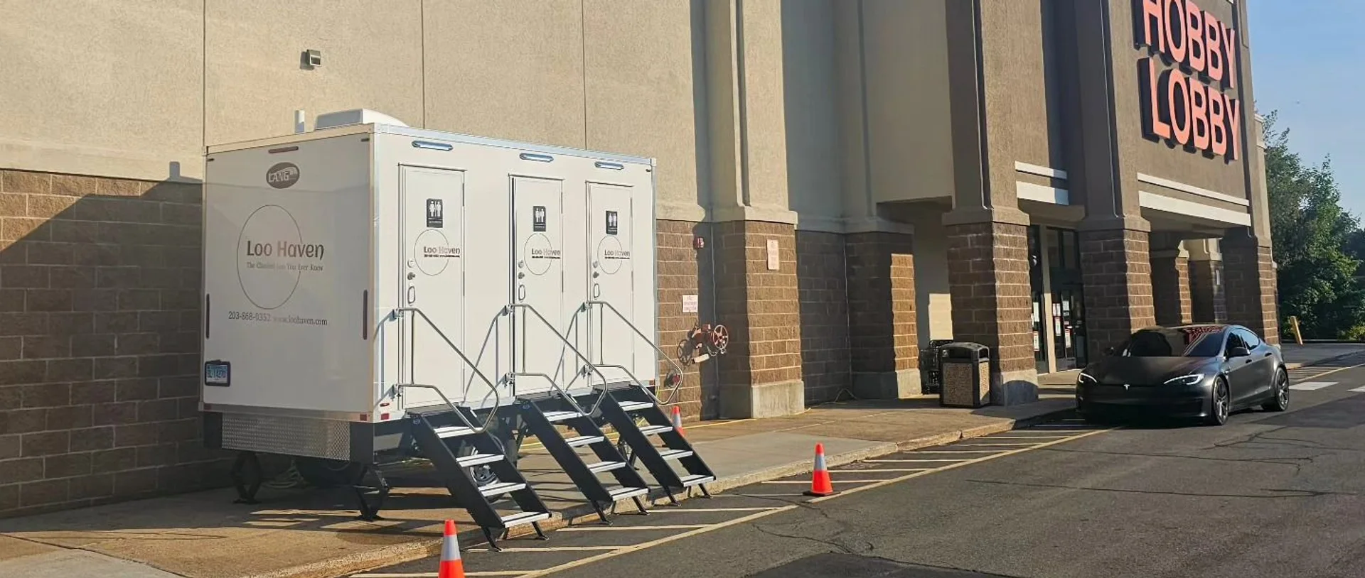 A three-stall Loo Haven restroom trailer set up with steps and safety cones on a commercial site